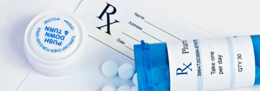 A blue prescription drug bottle spilled out on top of a prescription pad. 