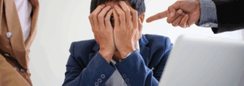 man with his hands over his eyes being bullied by other employees