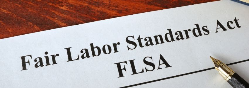 Fair Labor Standards Act (FLSA) typed on top of a piece of paper with a pen sitting to the side.