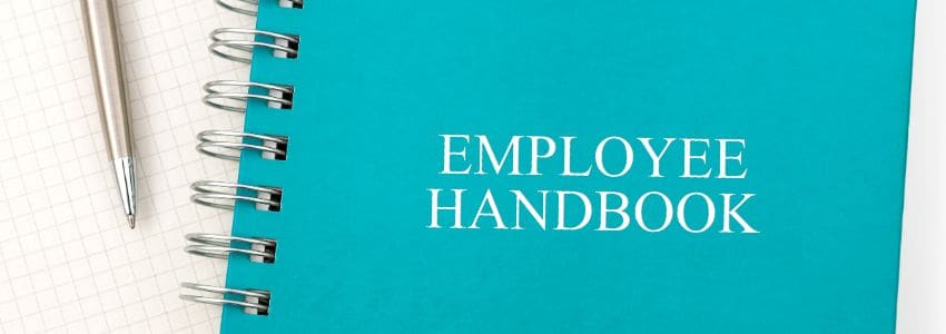 A blue spiral bound handbook with "employee handbook" with a pen beside it