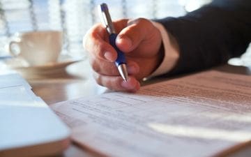 View of a man's hand holding a pen reviewing an HR document, representing HR Compliance & Recordkeeping Services- part of our Outsourced HR Solutions