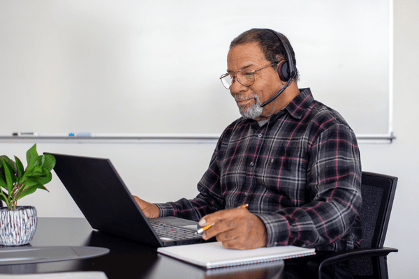 Contract HR professional sitting at a desk working on their laptop while talking on a headset.