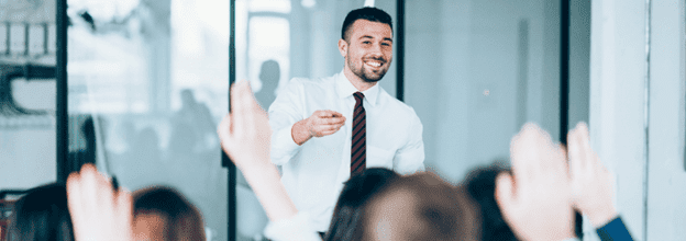 Individual training a group of individuals with their hands up discussing trends